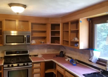 Unpainted kitchen cabinets with open shelves and masking in place around counters and window in Billerica kitchen