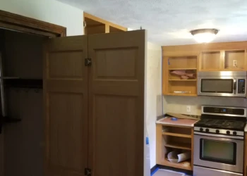 Partially refinished kitchen cabinets with no doors in a Billerica home showing cabinet frames and stainless steel stove and microwave.