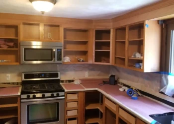 Unfinished wooden kitchen cabinets and drawers with countertops covered, undergoing refinishing work in Billerica MA kitchen