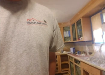 Worker wearing Finish Masters Builders Corp shirt beside partially stripped kitchen cabinets in Billerica MA