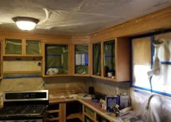 Kitchen cabinets with protective plastic and masking tape throughout for refinishing in Billerica MA