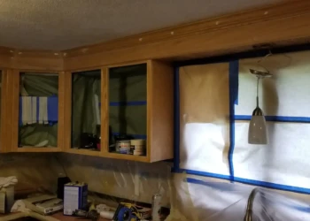 Kitchen cabinets with glass doors and wood trim covered for refinishing preparation in Billerica MA
