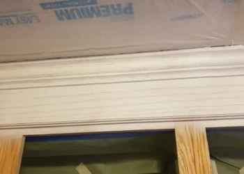 Close-up view of light off-white kitchen cabinet doors with wood grain texture and protective covering above
