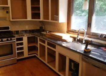Kitchen with cabinets missing doors and drawers, showing open cabinetry and black countertop under daylight in Billerica home