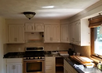 Repainted kitchen cabinetry and drawers in off-white with granite countertop and natural light through window.