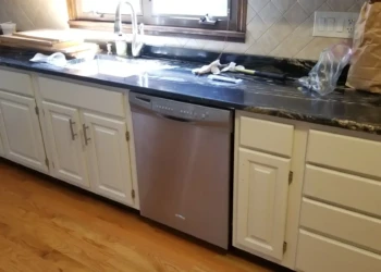 Long row of painted off-white kitchen cabinets with stainless steel dishwasher and dark granite countertop in a Billerica kitchen