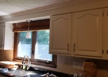 Off-white painted kitchen cabinets with raised panel doors above a kitchen sink with window in Billerica home