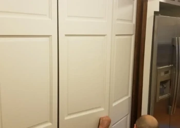 Off-white painted linen closet doors in a kitchen area next to stainless steel refrigerator