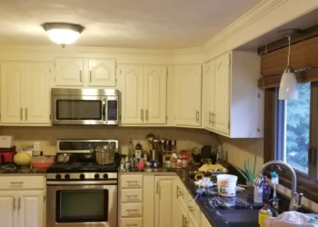 Kitchen cabinets painted in light off-white color with stainless steel appliances and black countertops in Billerica kitchen