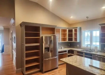 Empty kitchen cabinets and stainless steel refrigerator in a North Andover kitchen before refinishing