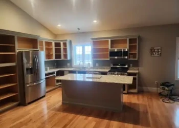 Empty kitchen with hardwood floor, gray island, and unpainted open cabinets ready for cabinet painting in North Andover MA
