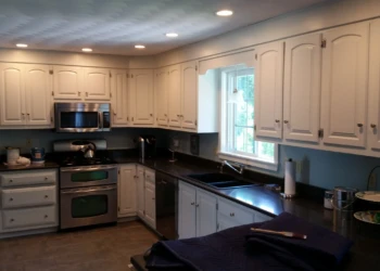Freshly painted white kitchen cabinets with many doors and drawers under window with dark countertops in North Andover kitchen