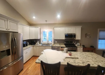 L-shaped kitchen with white painted cabinets, granite countertops, stainless steel appliances, and hardwood floor