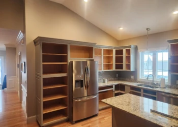 Kitchen cabinets in mid-refinishing stage with no doors installed around stainless steel refrigerator in North Andover MA kitchen