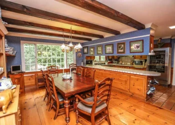 Dining area with large pine flooring and refinished pine kitchen cabinets in Bedford NH kitchen with blue patterned wallpaper and wooden beams