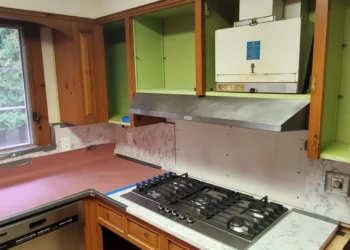 Kitchen cabinets stripped and prepped for refinishing around gas cooktop and stainless dishwasher in Bedford NH kitchen