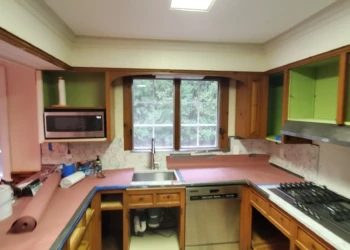 Kitchen with stripped wood cabinets and protective covering on countertops during cabinet painting preparation in Bedford NH