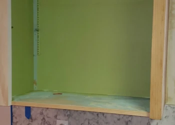 Open kitchen cabinet frame with green interior and wood trim, prep materials on countertop below in Bedford NH kitchen