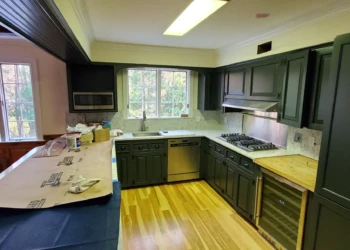 Kitchen with dark painted cabinets, butcher block countertop, stainless steel appliances, and large windows illuminating hardwood floor in Bedford NH