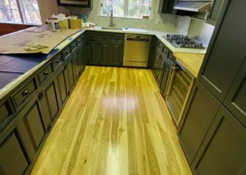U-shaped kitchen with dark green refinished cabinets, light polished wood floors, stainless appliances, and butcher block countertop in Bedford NH
