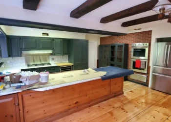 Kitchen interior with dark green refinished cabinets, wooden island, brick accent wall, and stainless steel appliances in Bedford NH