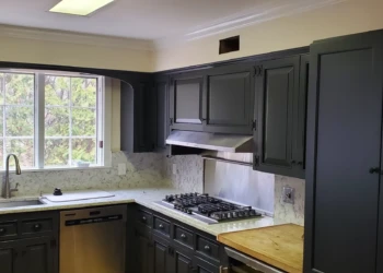 Dark gray painted kitchen cabinets with gas cooktop and stainless steel appliances under natural light in Bedford NH kitchen