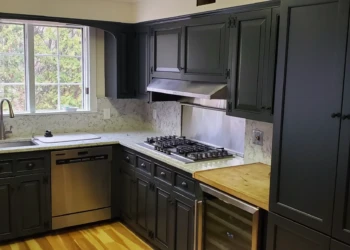 L-shaped kitchen with dark painted cabinets, light marble countertops, a stainless steel stove and dishwasher, and wooden flooring in Bedford NH