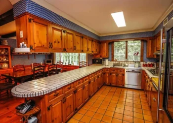 Bedford NH kitchen featuring refinished pine cabinets, tiled countertops, terracotta floor tiles, and wooden dining area