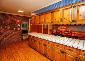 A kitchen with refinished pine cabinets, white tiled countertop, terracotta tile floor, and brick wall in Bedford NH