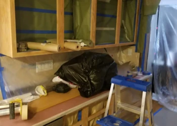 Kitchen cabinets with open doors and protective plastic sheeting taped around, captured during refinishing prep in Billerica MA