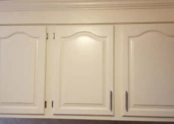 Smooth, light off-white painted kitchen cabinet doors with brushed metal handles and detailed molding.
