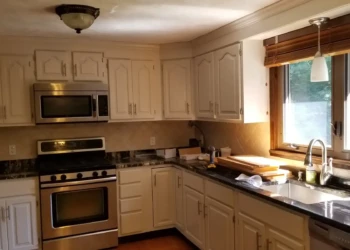 Refinished kitchen cabinets in off-white color with stainless steel appliances and black granite countertops in Billerica home