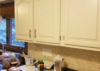 Off-white painted kitchen cabinets with modern hardware above black countertop near window