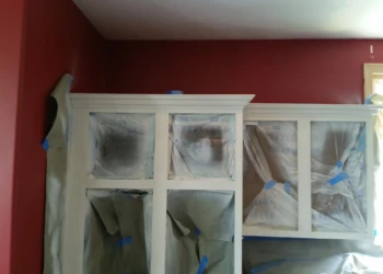 Kitchen cabinets in the process of priming with protective plastic covers on cabinet interiors in Carlisle, MA kitchen