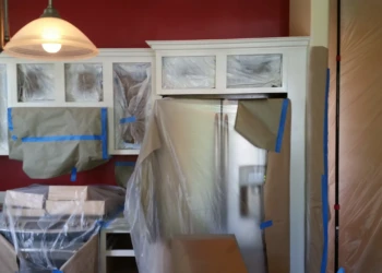Kitchen cabinets and appliances covered and masked for protective priming during cabinet refinishing in Carlisle MA