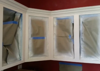 Close-up of kitchen cabinet frames with protective paper and blue painter’s tape during priming stage in Carlisle MA kitchen cabinet refinishing project