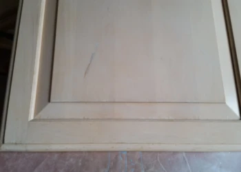 Close-up of a light-colored cabinet door with visible cracks and chips prior to refinishing in Carlisle MA