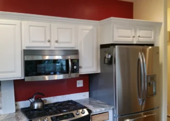 White kitchen cabinets refinished with a red wall background and stainless steel microwave and refrigerator in Carlisle MA kitchen