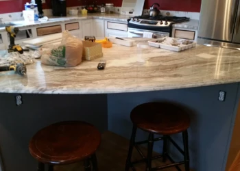 Polished marble kitchen island countertop with dark gray base and two wooden stools in a Carlisle kitchen