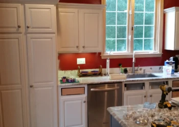 White kitchen cabinets and a kitchen island in mid-refinishing with some cabinet doors removed and tools on the countertop in Carlisle MA