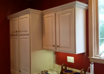 Cream-colored kitchen cabinets refinished with crown molding above near a window in Carlisle MA kitchen