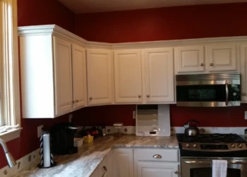 White painted kitchen cabinets with repaired doors above marble countertop near window and stainless steel appliances in Carlisle kitchen