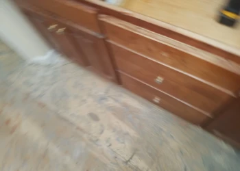 Blurry photo of lower kitchen cabinets and drawers in need of refinishing on a bare floor in Carlisle MA
