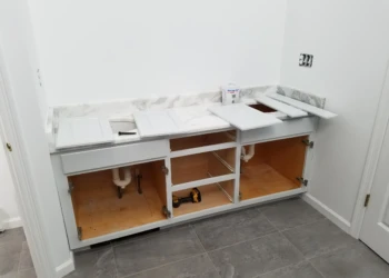 Partially refinished white kitchen cabinets with open doors and detached panels under marble countertop in Carlisle MA