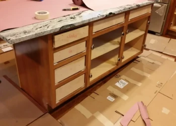 Wood kitchen island with doors and drawer fronts removed for cabinet refinishing in Concord MA by Finish Masters Builders Corp.