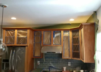 Kitchen cabinets being refinished with protective plastic on the glass doors.
