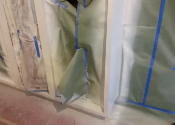 Cabinet refinishing in progress with masking tape and protective coverings.