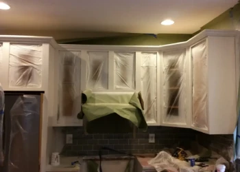 Kitchen cabinets being refinished with protective masking and plastic covering.