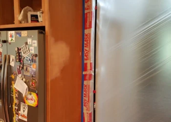 Wood kitchen cabinets near a refrigerator with protective plastic sheeting taped for refinishing prep in Groton MA