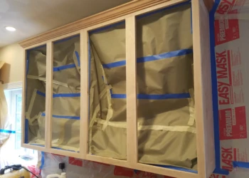 Wood kitchen cabinet frames covered with protective paper and tape in a Groton MA home during refinishing preparation